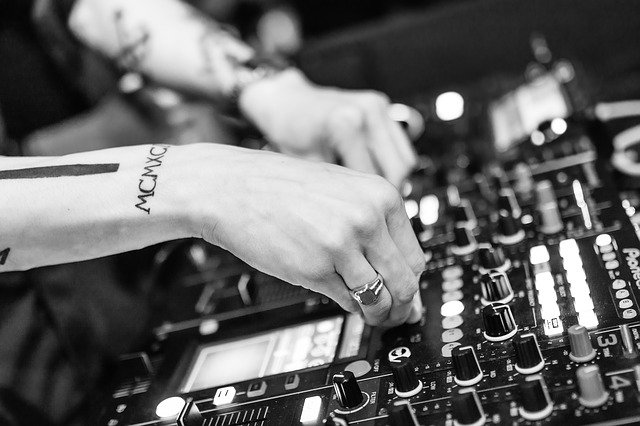 person with tattoos on their arms adjusting the knobs of a mixing board